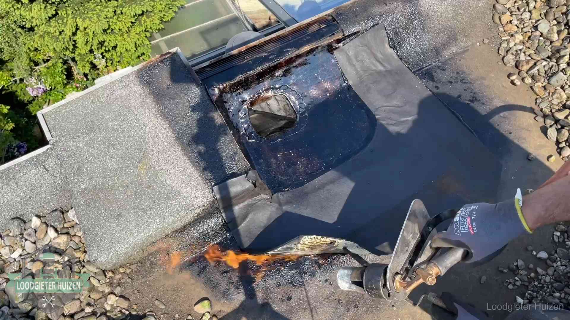 Daklekkage repareren in Huizen Dakdekker brandt bitumen rond een doorvoer tijdens een daklekkage-reparatie in Huizen