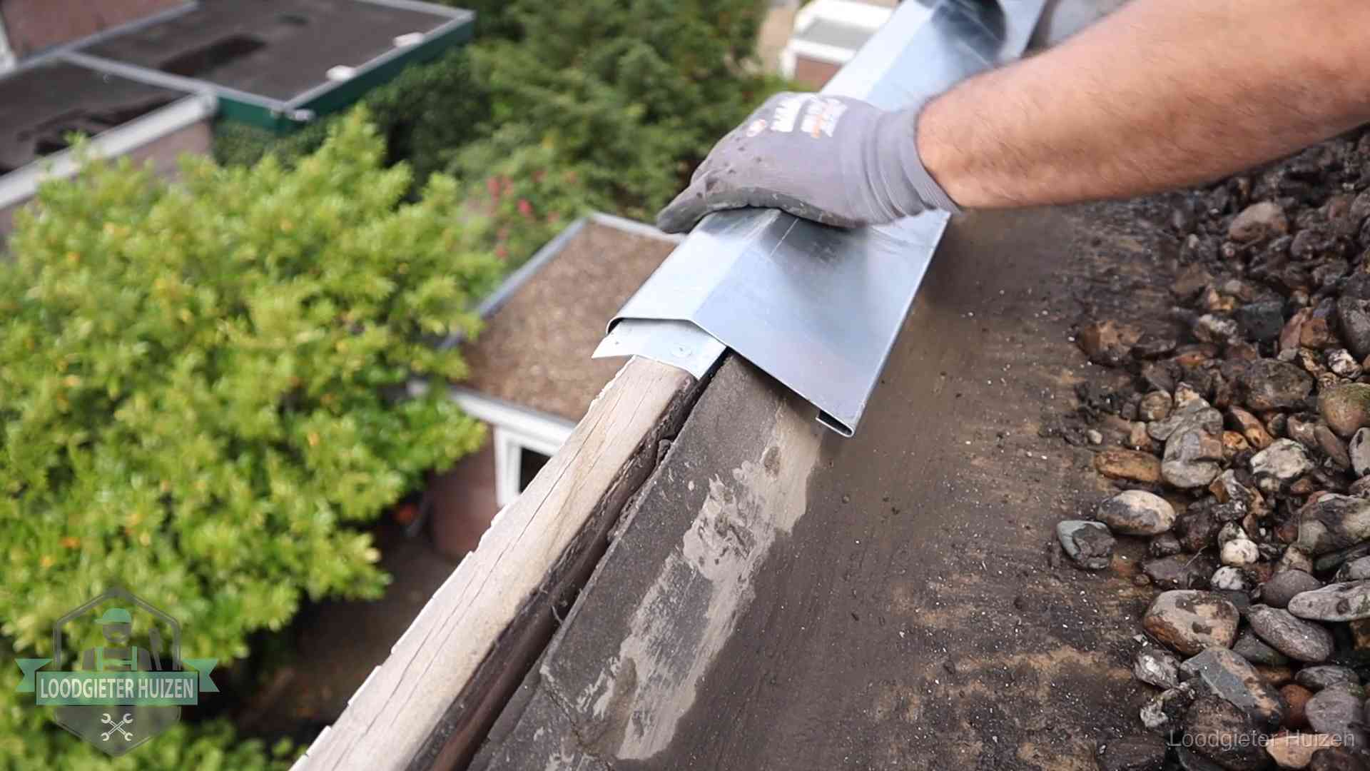 Daklekkage per wijk in Huizen Dakdekker plaatst een zinken deklijst op een dakrand met uitzicht over een woonwijk in Huizen
