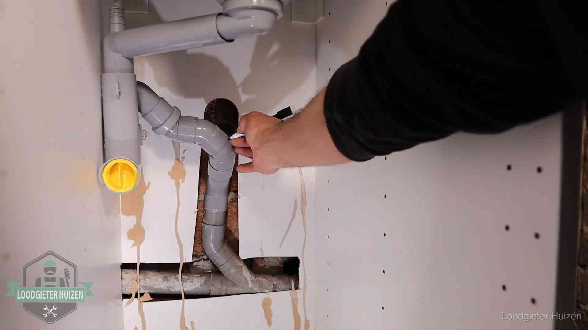 Loodgieter voor verhuurders en bedrijven in Huizen Loodgieter markeert een pvc-afvoerbuis onder een gootsteen in Huizen