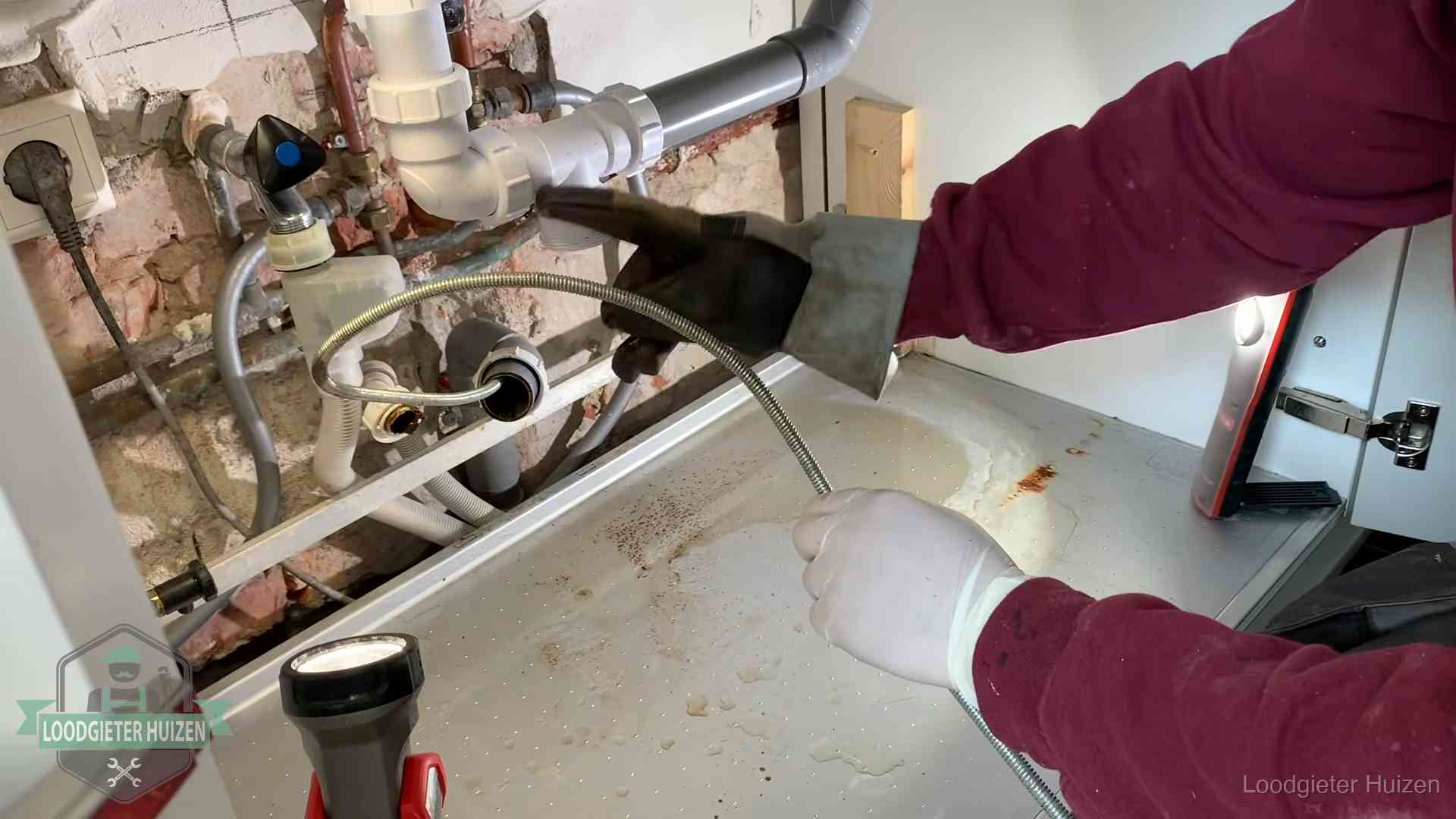 Ontstoppingsveer gaat in een geopende sifonaansluiting onder het aanrecht in Huizen