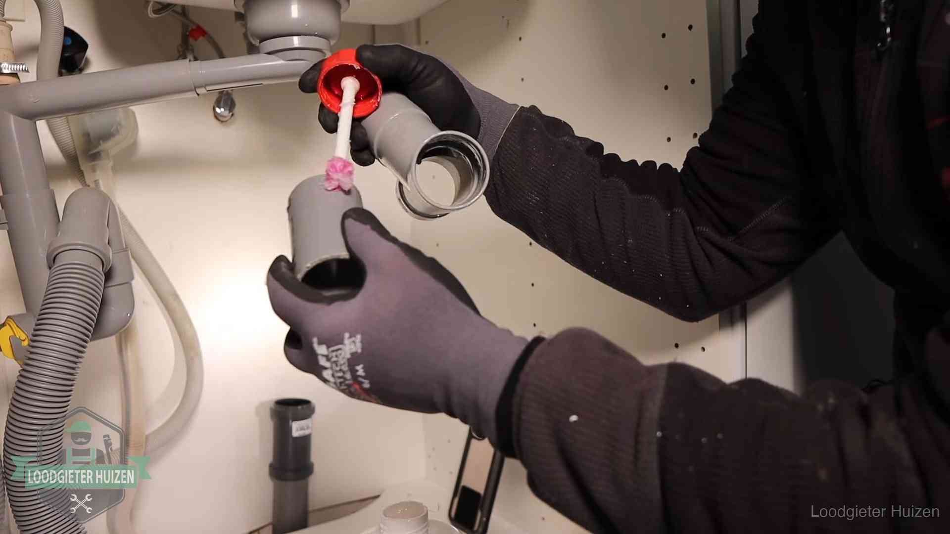 Loodgieter demonteert en reinigt de sifon onder een keukenkast in Huizen