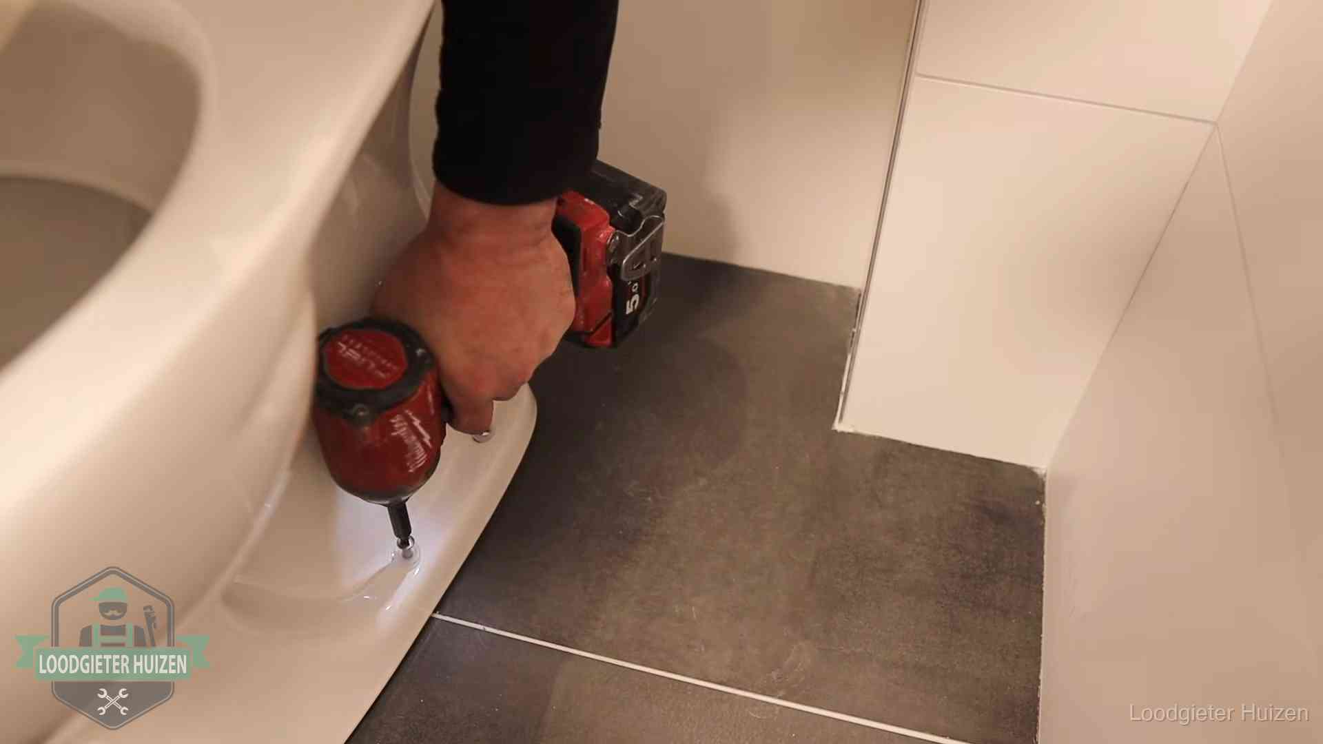 Kosten wc ontstoppen in Huizen Loodgieter zet de voet van een wc-pot vast op de tegelvloer in Huizen